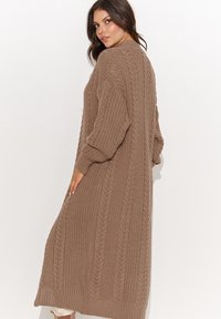 Sweter kardigan w jasnobrązowym kolorze z fakturowanym wzorem w warkocze, z długimi rękawami i luźnym krojem, sięgający poniżej kolan, z prążkowanymi wykończeniami.