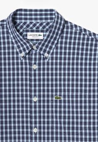 Camicia a quadri blu navy e azzurro chiaro con colletto classico, bottoni bianchi e logo di coccodrillo ricamato sul taschino.
