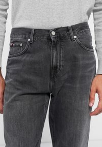 Graue Jeans aus Denim mit gerader Passform, ausgestattet mit einem Knopfverschluss, zwei vorderen Taschen und einem kleinen Markenakzent auf der linken Tasche.