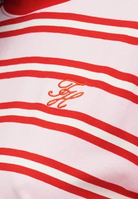 Κόκκινη και λευκή ριγωτή μπλούζα από βαμβάκι, με κεντημένο πορτοκαλί λογότυπο, στρογγυλή λαιμόκοψη και απαλό υφασμάτινο ύφασμα.