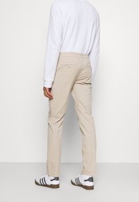 Béžové kalhoty v rovném střihu, se zadními kapsami na knoflíková zapínání. Nosit s bílým dlouhým rukávem a bílými teniskami.