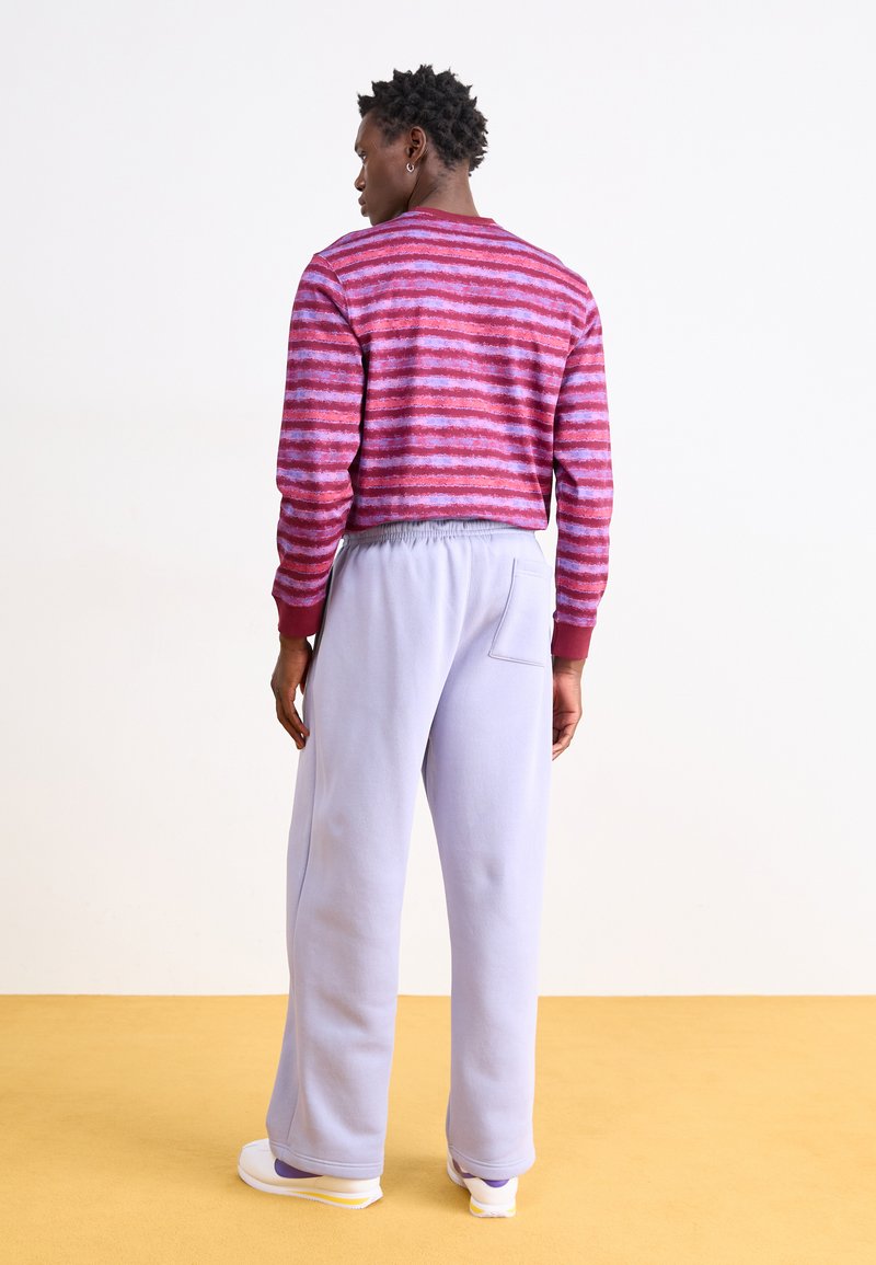 Pull rayé dans des tons rouges et violets avec des poignets côtelés, associé à un pantalon de survêtement violet clair avec une poche au dos.