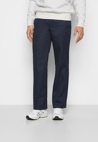 Navy blue trousers made of smooth fabric, featuring a straight-leg design and minimal stitching details, paired with white athletic shoes.