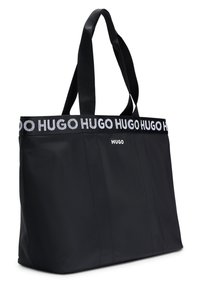 Borsa tote nera realizzata in tessuto morbido, dotata di due manici robusti e di una banda con il logo HUGO bianco ben visibile nella parte superiore. Design semplice e rettangolare.