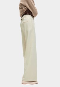 Wijdvallende broek in lichtcrème stof, met een hoge taille, strakke lijnen en subtiele achterzakdetails. Gladde textuur, minimalistisch ontwerp.