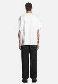 Przesadnie duża biała koszulka bawełniana z opadającymi ramionami, w połączeniu z czarnymi luźnymi dżinsami z kontrastowym szwem na tylnej kieszeni.