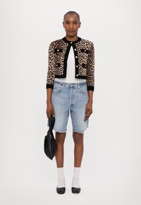 Cardigan scurt cu model leopard și accente negre, tricou alb, pantaloni scurți din denim deschis, șosete pentru gleznă și pantofi plate negri, ținând o geantă neagră.