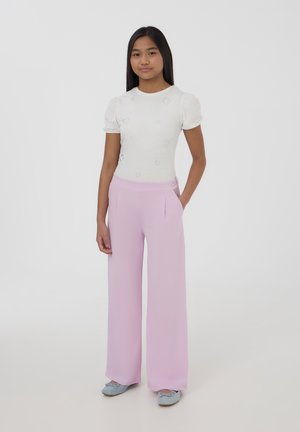 Top bianco a maniche a puff con decorazioni a forma di cuore abbinato a pantaloni a gamba larga rosa chiaro a vita alta. Le scarpe sono blu con fiocchi.