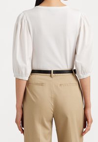 White puff-sleeve top with a crew neckline, paired with beige tailored pants featuring side pockets and a black belt. Smooth fabric texture.