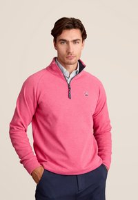 Lichtroze pullover van zachte stof, met een ritskraag, geribbelde manchetten en een klein logo op de borst.