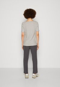 Camiseta gris con rayas y mangas cortas, combinada con pantalones gris oscuro y zapatillas deportivas, vista desde la parte posterior sobre un fondo blanco.