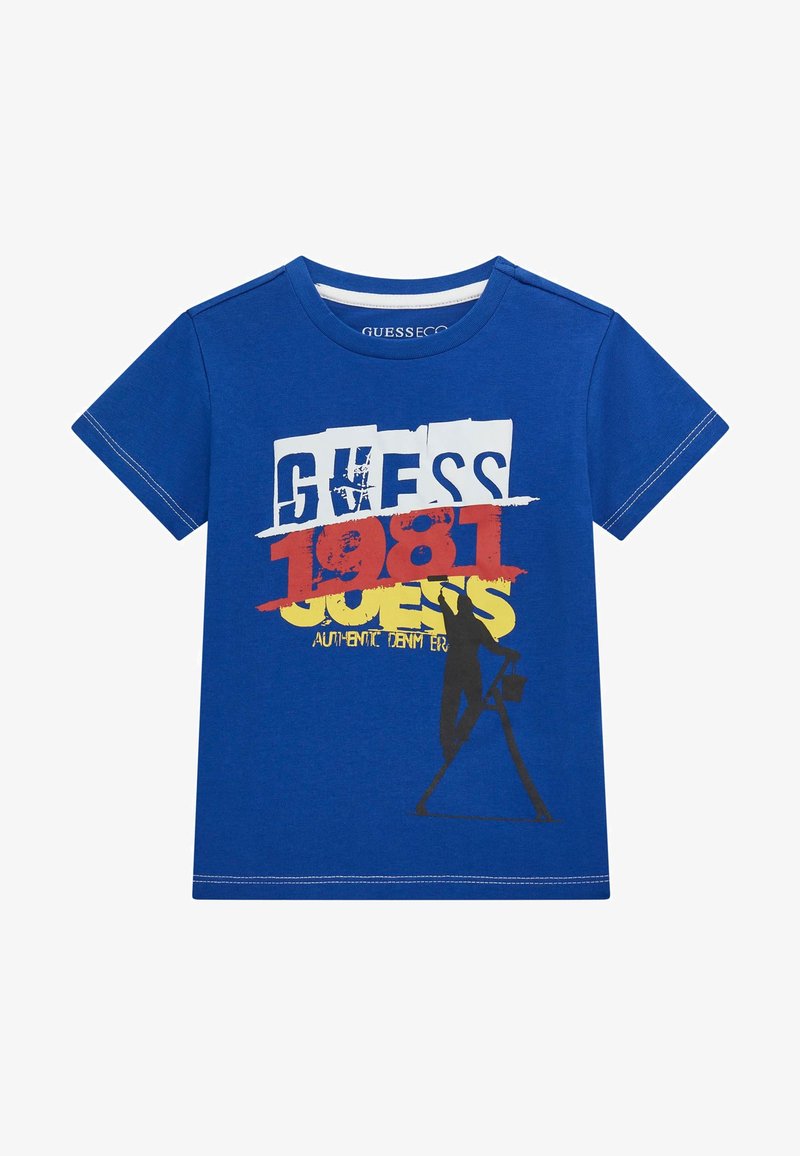 T-shirt in cotone blu con una grafica che presenta la scritta bianca "GUESS," rossa "1981," gialla "GUESS" e una silhouette nera di una persona con un secchio.