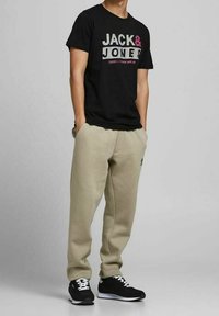 Černé bavlněné tričko s logem "JACK & JONES" v šedé a růžové; béžové tepláky; černé tenisky s bílými šňůrkami.