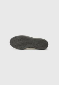 Svart gummisåle til sneakers med et strukturert grep mønster og logo. Har en glatt kant og lett krumming langs hælen.