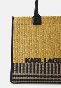 Tkaná slámová taška s žlutou horní částí, černými koženými akcenty a logem "KARL LAGERFELD" v černé barvě, s vodorovným pruhovaným vzorem na spodní části.