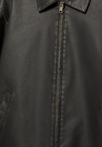 Czarna skórzana kurtka z przednim zamkiem błyskawicznym, kołnierzem i widoczną boczną kieszenią, ukazująca szczegółową fakturę skóry i szwy.