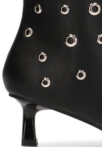 Botín de cuero negro hasta el tobillo con detalles de ojetes circulares plateados, puntera puntiaguda y un tacón bajo y cuadrado. Textura suave en toda la superficie.