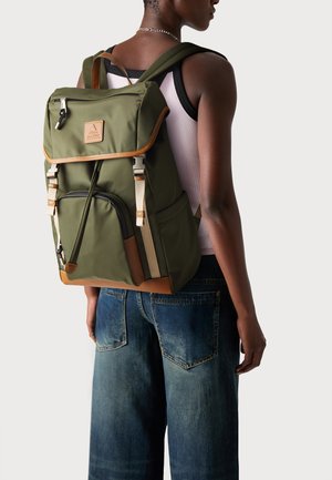 Mochila verde con un diseño estructurado, detalles en cuero, correas ajustables y un bolsillo frontal. Fabricada con un tejido duradero de acabado mate.