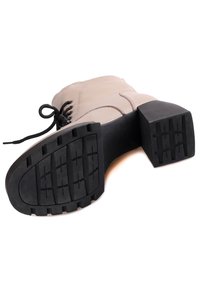 Stivale beige alla caviglia con design allacciato, caratterizzato da una suola in gomma nera spessa e un motivo rigato per una migliore aderenza.
