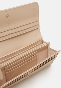 Beige lærte lommebok med flere kortlommer, glidelåsrom og preget logo. Glatt tekstur og strukturert design.