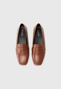Mocassins en cuir marron avec un design à orteil carré, présentant une sangle décorative et une semelle intérieure noire texturée. Nom de la marque "RAID" imprimé à l'intérieur.