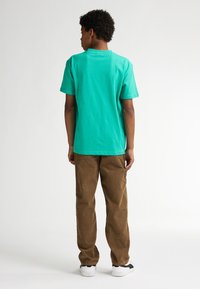 T-shirt in cotone turchese a maniche corte, abbinata a pantaloni in corduroy marroni. Sneakers bianche e nere, design semplice, vestibilità casual.