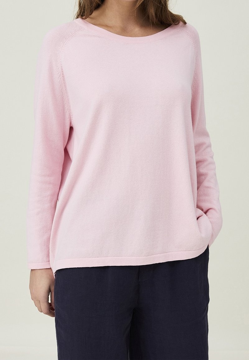 Ljusrosa långärmad tröja i mjukt material med en avslappnad passform, med vid halsringning och ribbade kanter. I kombination med mörka byxor.
