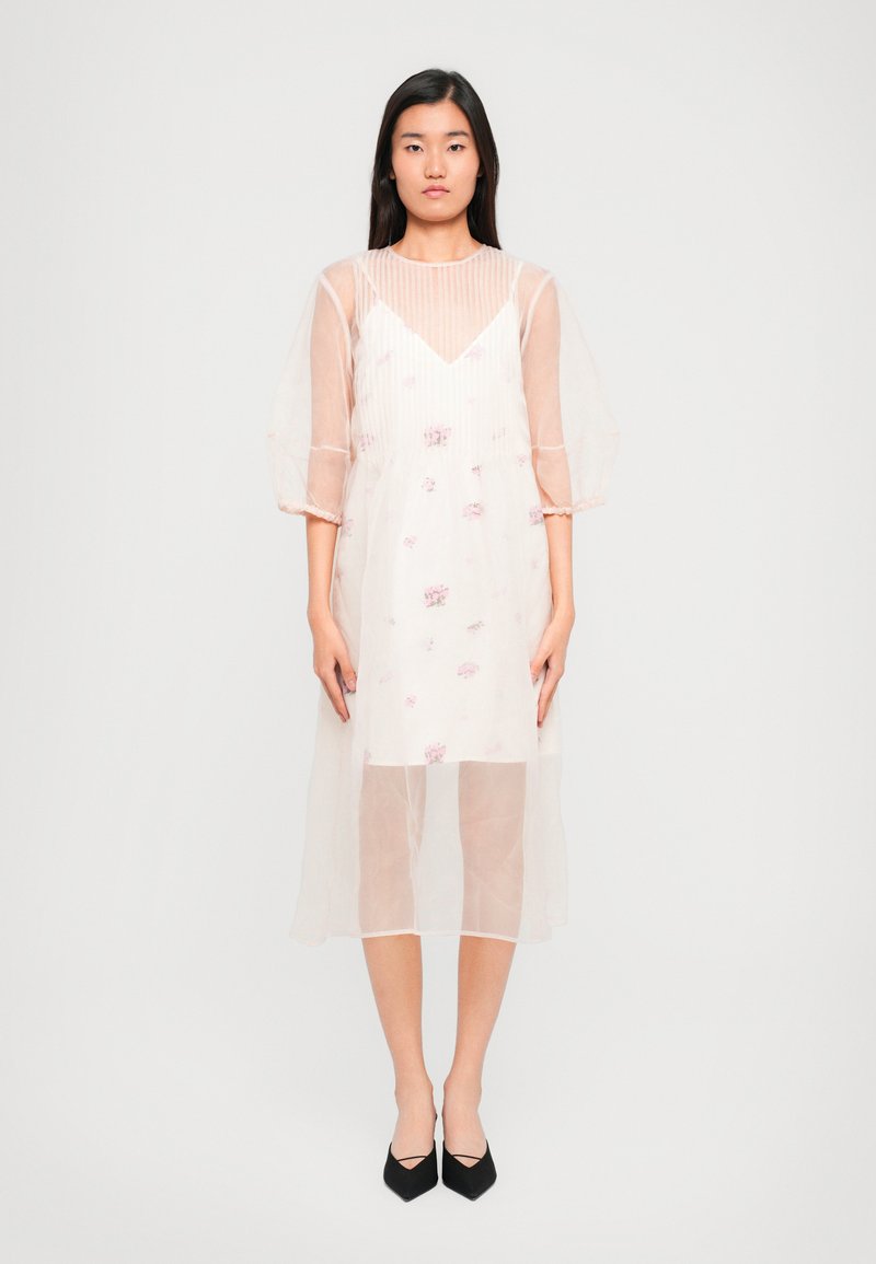 Áttetsző, világos rózsaszín ruha virágos hímzéssel, V-nyakkivágással és puffos ujjal. Többrétegű kialakítással és térd alatt végződik.