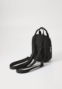 Sac à dos noir en tissu, de forme rectangulaire, avec deux poignées supérieures, des bretelles réglables portant le logo "TOMMY JEANS" et une fermeture éclair.