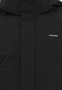 Mustmust must jacket, mille kaela ja valge logoga. Kanga pind on sile, ilma nähtavate mustrite või aksessuaarideta.