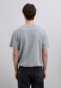 Graues Baumwoll-T-Shirt mit kurzen Ärmeln und rundem Ausschnitt, von hinten gesehen. Legere Passform, kombiniert mit dunklen Jeans.