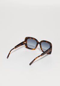 Gafas de sol de carey en forma cuadrada con lentes en degradado gris, patillas delgadas y detalles en dorado en el armazón, posicionadas en un ángulo.