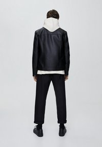 Svart läderjacka med en huva, bärs med en vit sweatshirt under, kombinerad med lösa svarta byxor och svarta sneakers. Slät textur, minimalistik design.
