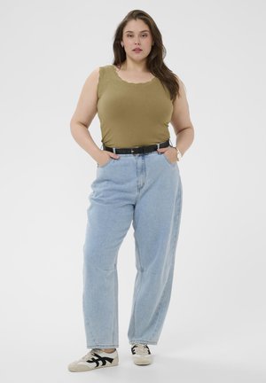 Mladá žena s dlhými hnedými vlasmi, oblečená v olivovom tielku bez rukávov, svetlomodrých džínsach s vysokým pásom, čiernym opaskom a bielymi teniskami.