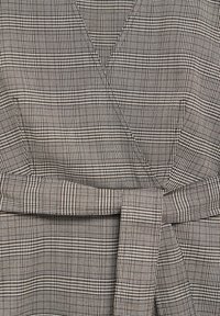 Sukienka kopertowa w czarno-białą kratę, wykonana z teksturowanej tkaniny, z wiązanym paskiem podkreślającym talię.