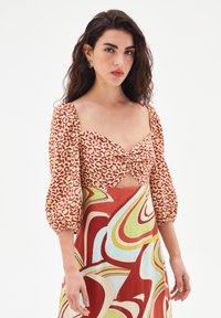 Haut à motif rouge et doré avec des manches bouffantes et un décolleté en cœur, associé à une jupe à motif ondulé multicolore.