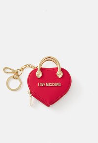 Raudona širdies formos raktų pakabuko piniginė su auksiniu metaliniu rankenėle, užtrauktuko uždarymu ir "LOVE MOSCHINO" įspaustu priekyje. Į komplektą įeina grandinėlė ir raktų žiedas.