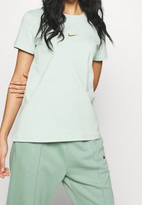 Ljusgrön bomullst-shirt med korta ärmar och rundhals, med en liten guld Nike-logga på bröstet.