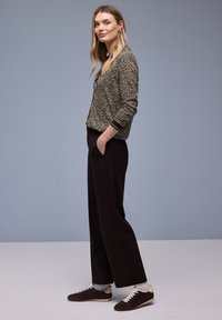 Veste à imprimé léopard noir et beige avec col et poignets côtelés, associée à un pantalon noir taille haute et des baskets marron.