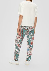 Biała bawełniana koszulka z krótkim rękawem w połączeniu z zielonymi, wzorzystymi spodniami z kwiatowymi motywami w kolorach czerwonym, niebieskim i białym. Casualowe białe trampki.
