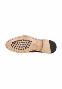 Vista inferior de la suela de un zapato, con una base de cuero marrón suave y puntos de goma negra para agarre, y una tapa de tacón negra. Logotipo grabado visible.