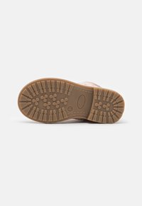 Stivaletto rosa per bambini con suola in gomma marrone che mostra un profondo motivo di battistrada e un'etichetta di dimensione 24, esposto su uno sfondo bianco.