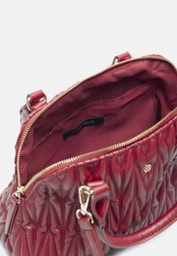 Czerwona pikowana torebka z błyszczącej skóry, złotym zamkiem i gładkim materiałowym wykończeniem. Wewnątrz znajduje się etykieta z logo oraz kieszonka.