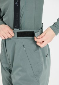 Grå utomhusbyxor med justerbara remmar, som har en slät fabrikkvalitet, kardborrestängning och fickor med dragkedja på sidorna.