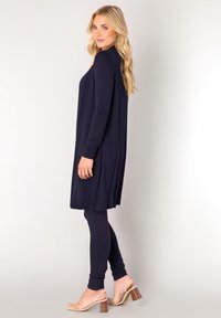 Marineblauwe tuniekjurk met lange mouwen, gecombineerd met bijpassende leggings. Zachte, rekbare stof met een ontspannen pasvorm, aangevuld met lichte nude enkelsandalen met hak.