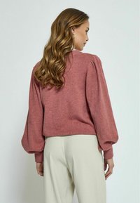 Puffed sleeve, cropped sweater in soft rose fabric. Textured knit with ribbed cuffs and hem. Paired with light-colored trousers.