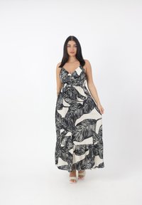 Robe maxi crème avec un motif de feuilles noires. Dispose d'un décolleté en V, de bretelles réglables et d'un ourlet à volants. Fabriquée en tissu léger.