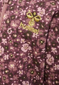 Veste zippée florale en violet, ornée de petites fleurs roses et vertes, logo "hummel" doré, texture douce et tissu côtelé.