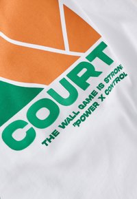 Maglietta in tessuto bianco con una grande grafica arancione e verde con la scritta "COURT" e altre frasi in verde sotto.