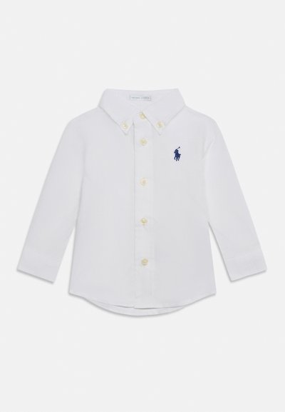 Λευκό παιδικό πουκάμισο με μακριά μανίκια, γιακά με κουμπιά και κουμπιά στο μπροστινό μέρος, με μικρό σκούρο μπλε κεντημένο λογότυπο παίκτη πόλο στο στήθος.